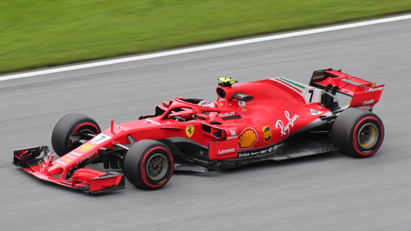 Red Ferrari SF71H with car number 7 and a halo over the cockpit, on track beside grass