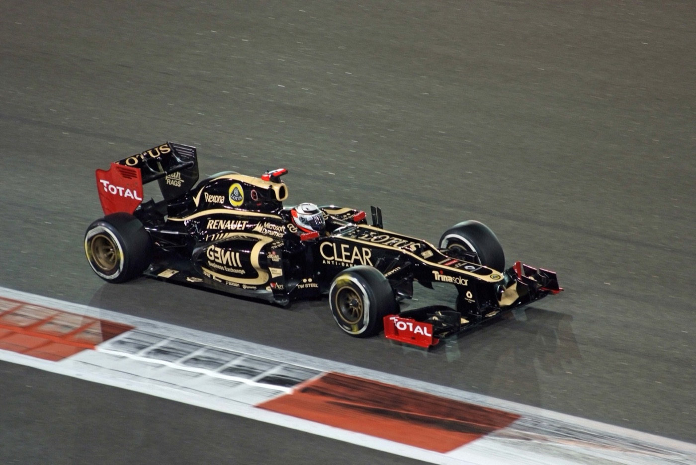 Black and gold Lotus E20 with red Total wings on a floodlit track at night