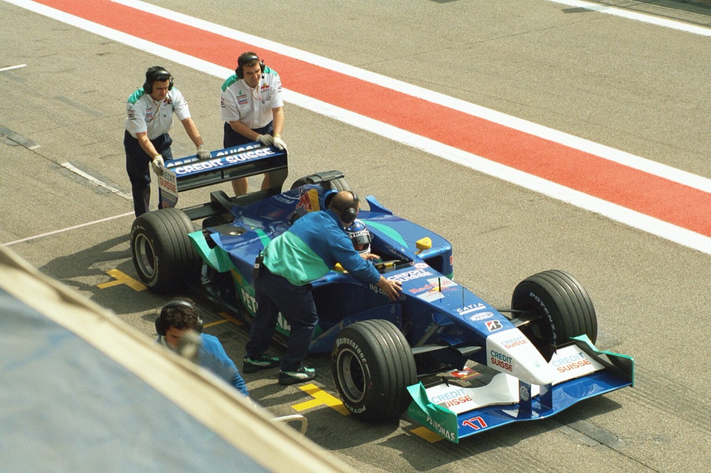 Blue and white Sauber C20 number 17 being pushed back into its garage by mechanics in the pit lane