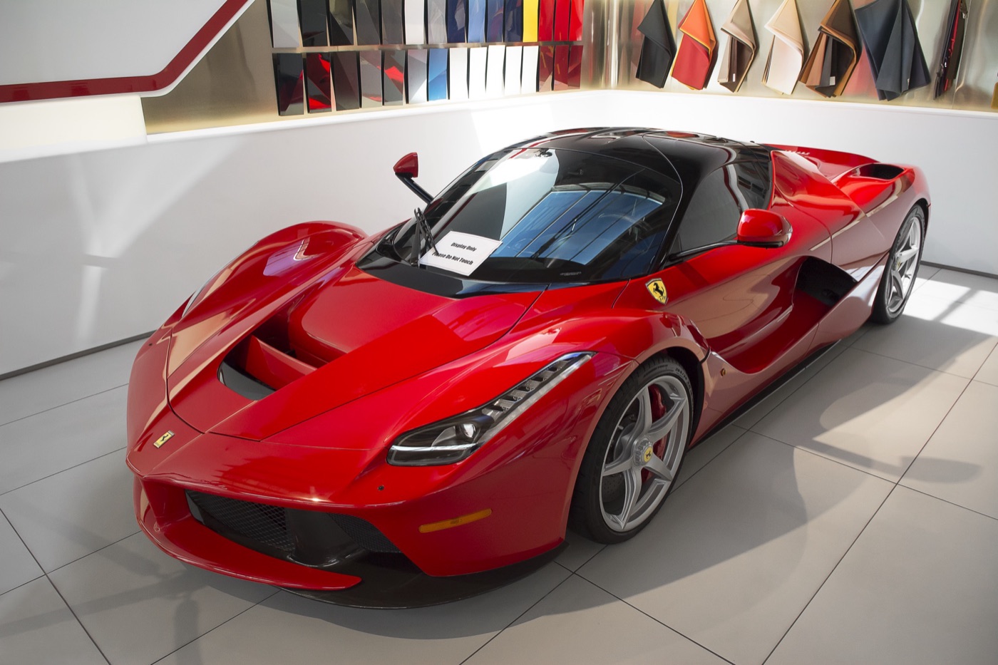 Red LaFerrari with a black roof, butterfly-door coupé shown from the front right inside a Ferrari showroom