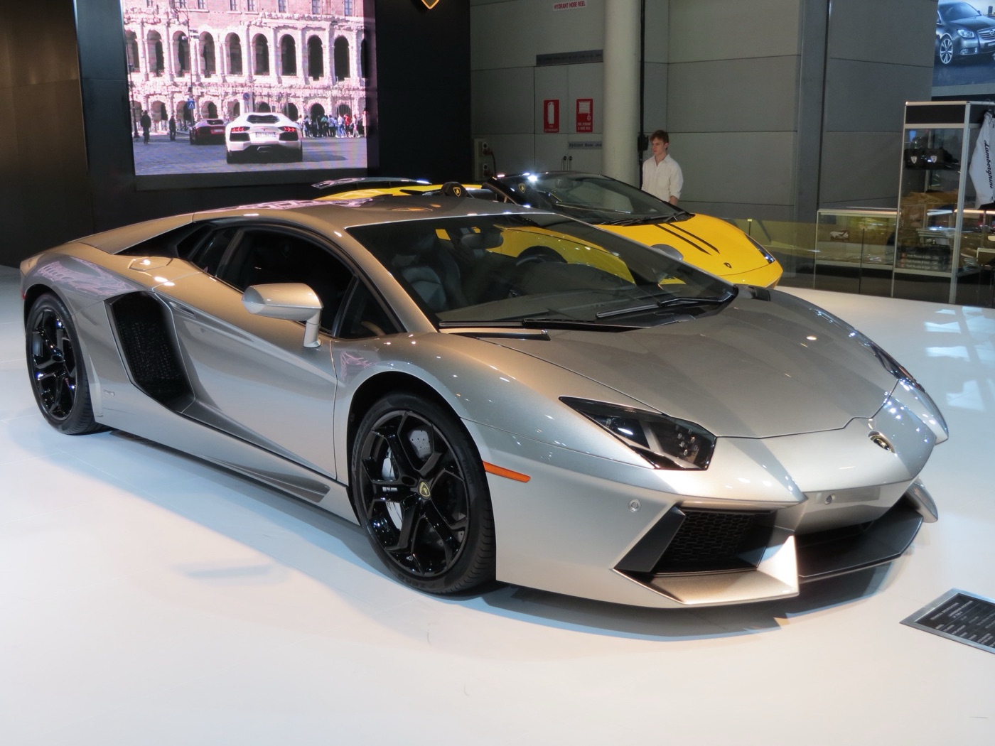 Silver Lamborghini Aventador LP 700-4 coupé with black wheels, seen from the front three-quarter on a motor show stand