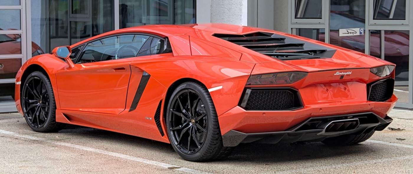 Orange Lamborghini Aventador LP 700-4 seen from the rear three-quarters, showing its engine cover louvres and black wheels