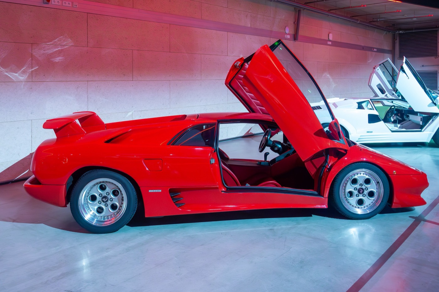 Red first-series Lamborghini Diablo seen from the side with its scissor door raised, in an indoor display hall