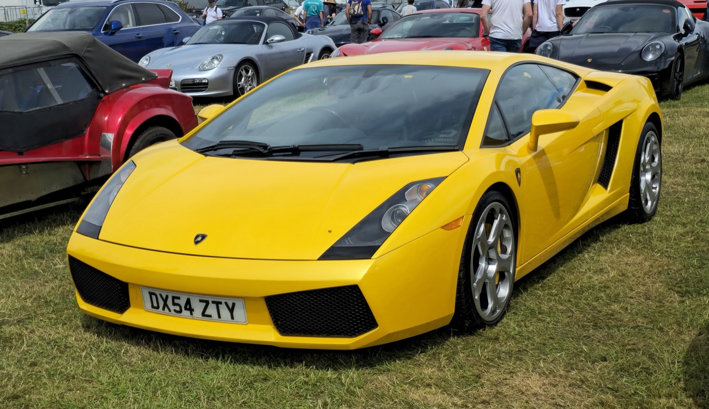 Yellow 2004 Lamborghini Gallardo coupé with silver wheels, parked on grass among other sports cars at a show