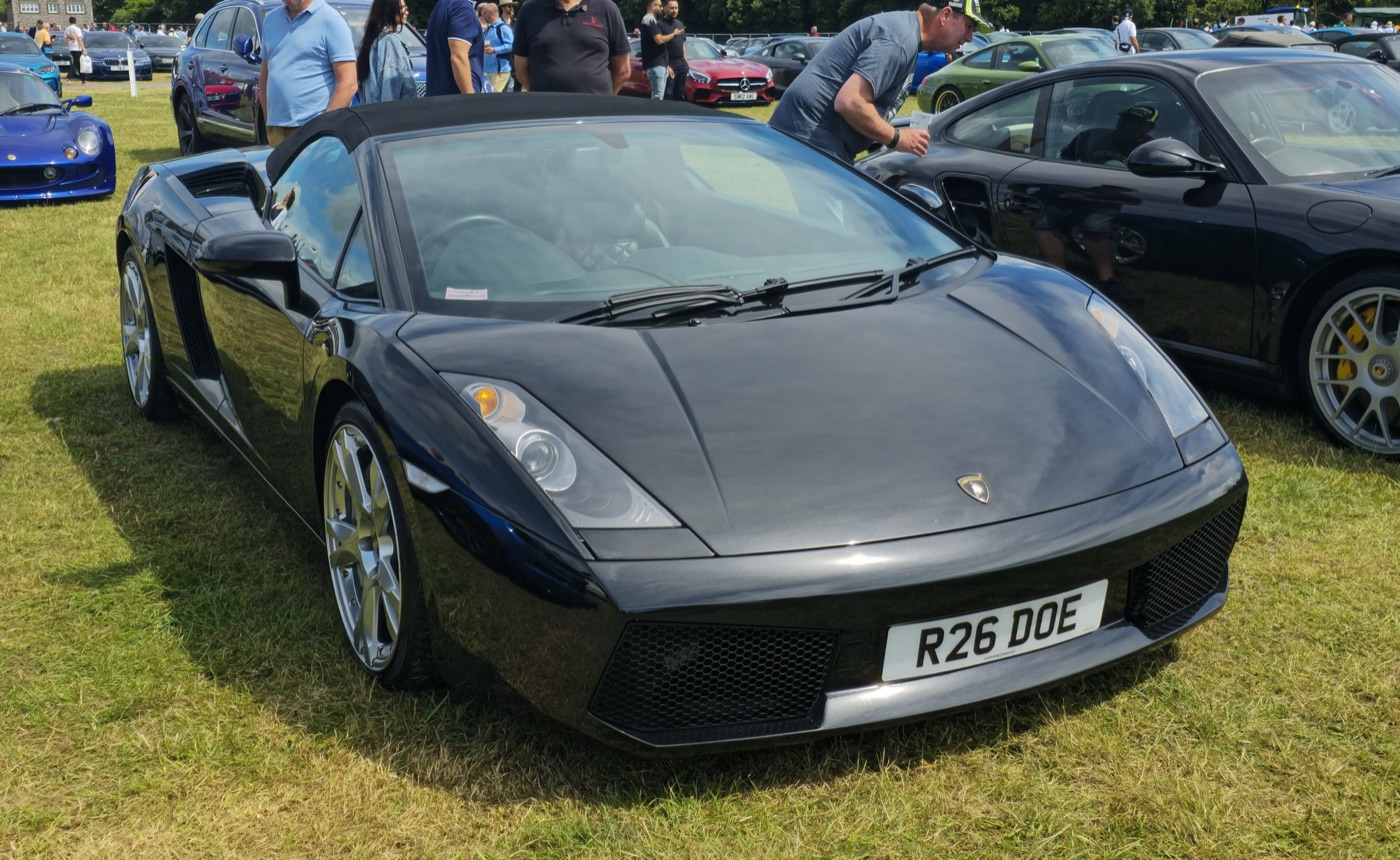 Black first-series Lamborghini Gallardo Spyder with its black fabric roof raised, parked on grass at a car show