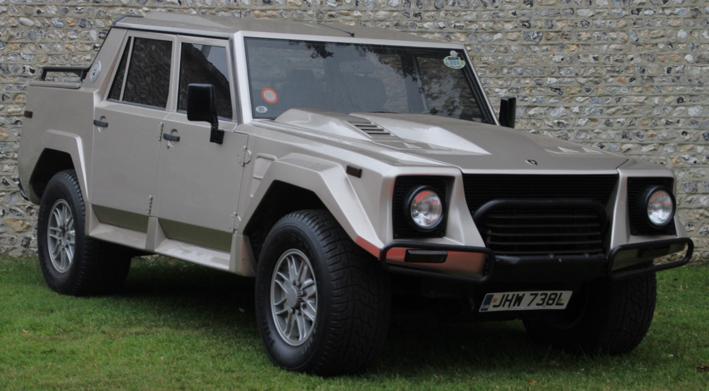 Champagne-coloured 1991 Lamborghini LM002 off-roader with a bonnet bulge and tubular bumpers on grass in front of a flint wall