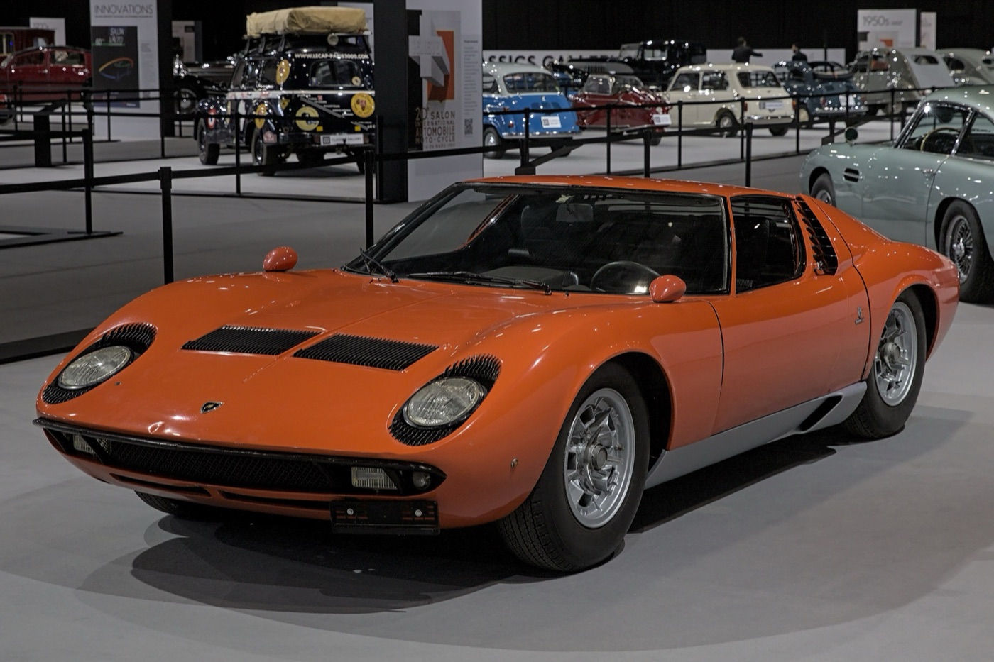 Orange Lamborghini Miura P400 S with black headlight eyelashes and bonnet vents on a motor show stand