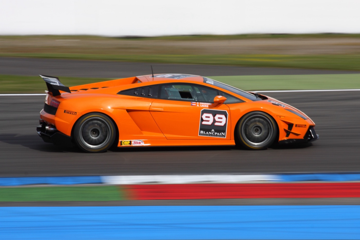 Orange Lamborghini Gallardo Super Trofeo race car number 99 panned at speed on a circuit, with blue and red kerbs in the foreground