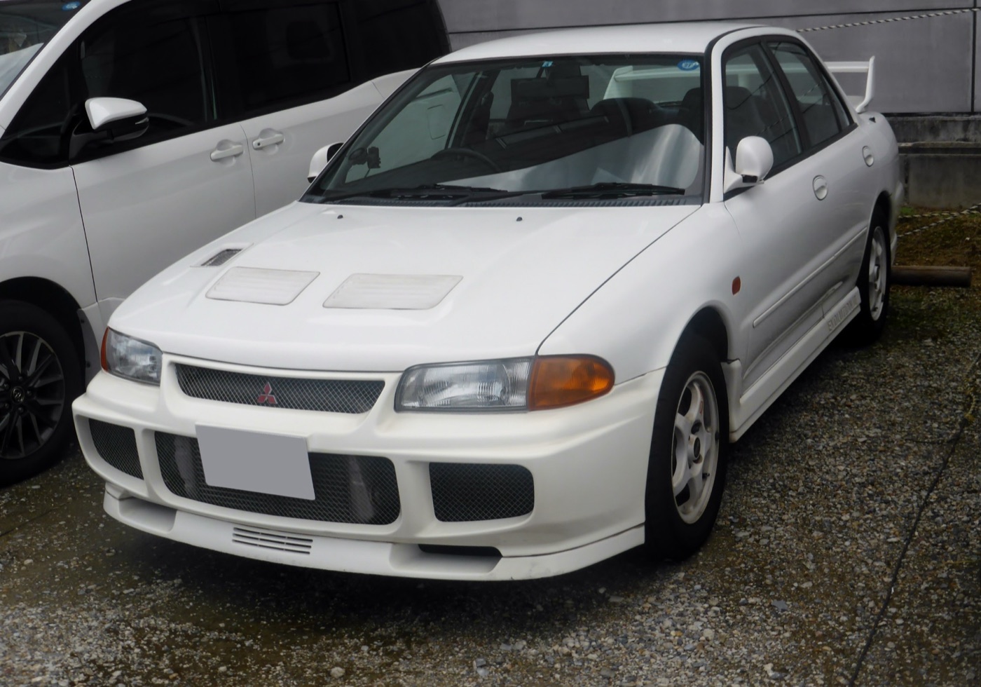 White Mitsubishi Lancer GSR Evolution III parked in Japan, showing its deep front bumper and rear wing