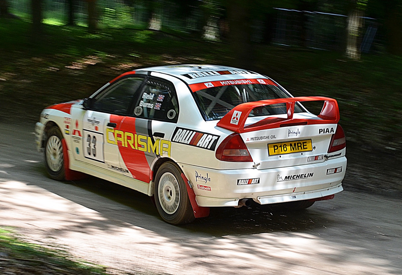 White and red Ralliart Lancer Evolution IV in Carisma GT livery with Burns and Reid names on the window, driven on the Goodwood forest rally stage