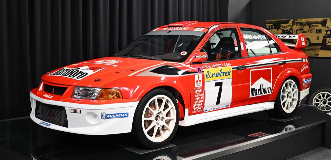 Red and white Marlboro-liveried Mitsubishi Lancer Evolution VI rally car number 7 on display, with Monte-Carlo rally plates