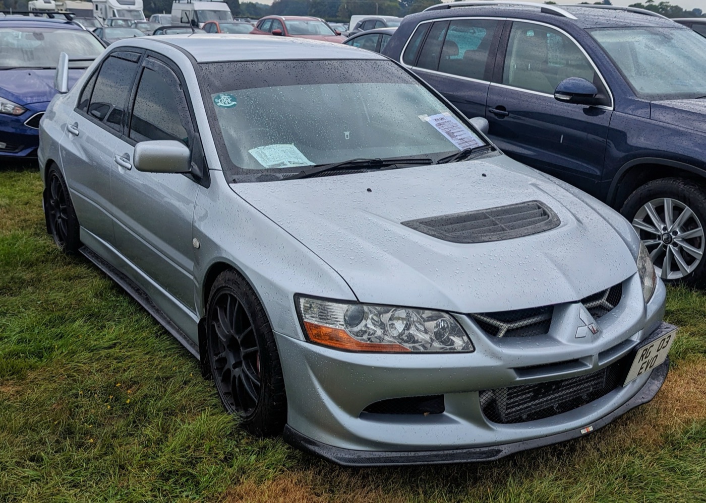Silver Mitsubishi Lancer Evolution VIII FQ-300 with a UK number plate parked on wet grass at a show