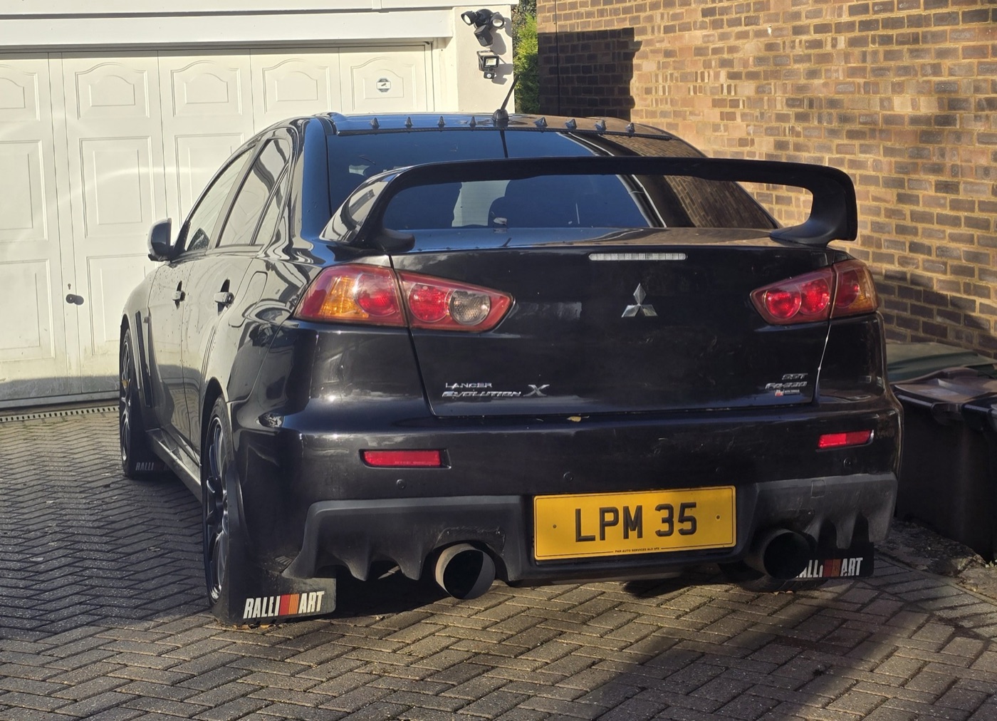 Black UK-registered Mitsubishi Lancer Evolution X with Ralliart mud flaps, seen from behind on a driveway