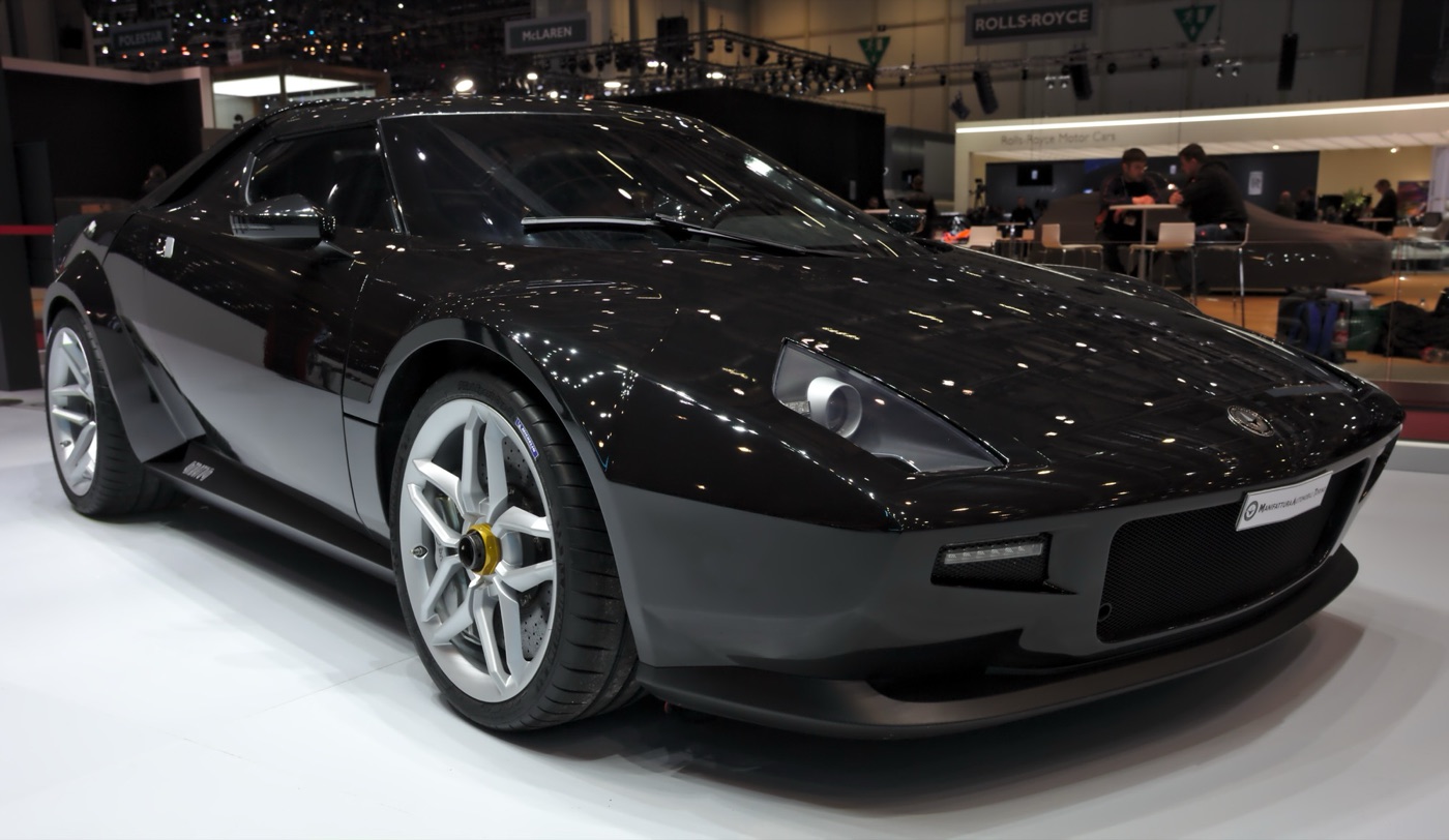 Black MAT New Stratos coupé with silver wheels and a wraparound windscreen on a motor show stand