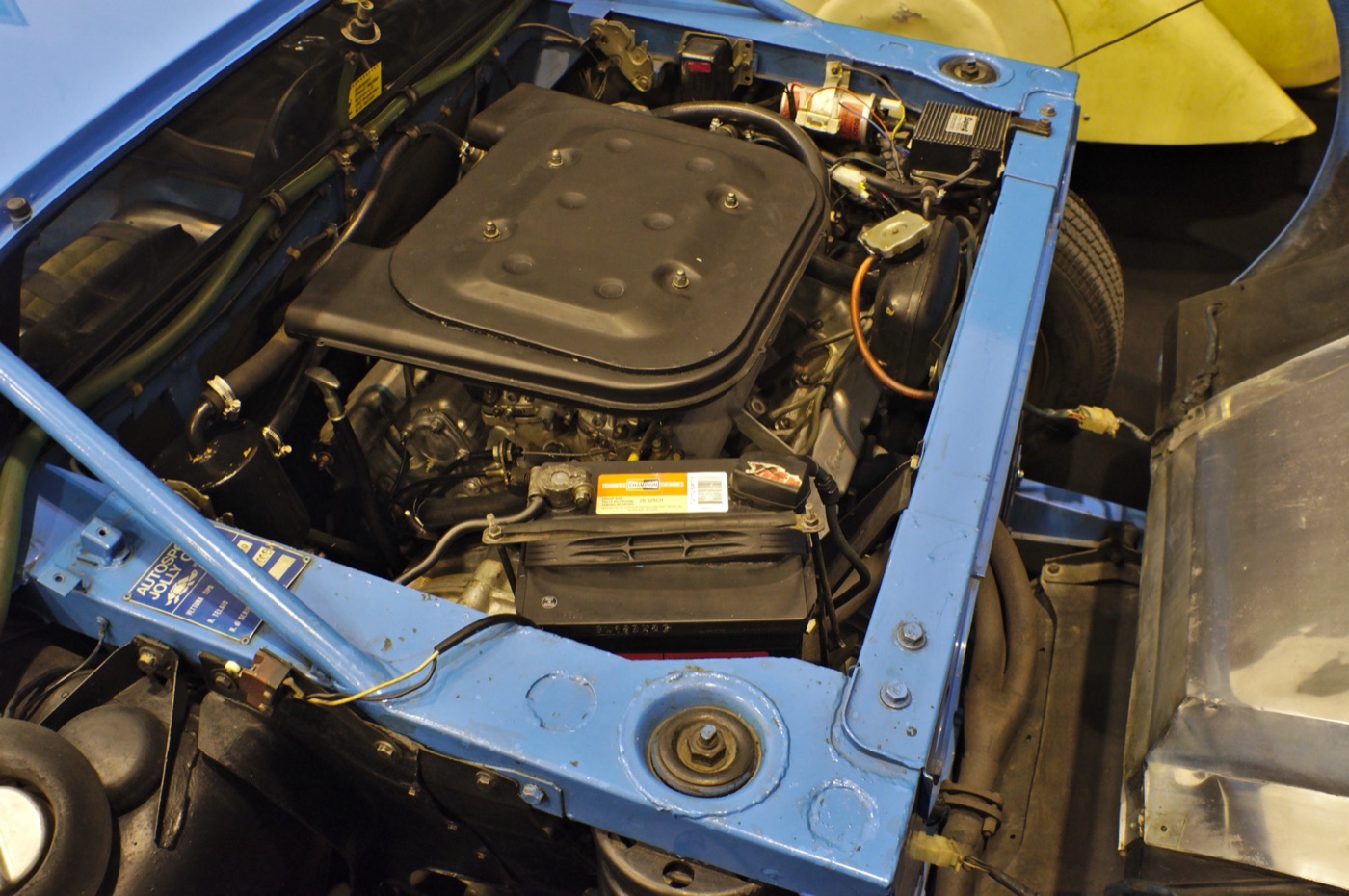 Engine bay of a blue Lancia Stratos Stradale, with the V6 under a black air box inside a blue steel frame