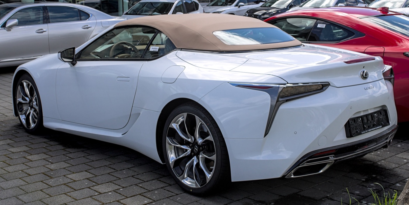 White Lexus LC 500 Convertible with a beige fabric roof, seen from the rear three-quarter on a dealer forecourt