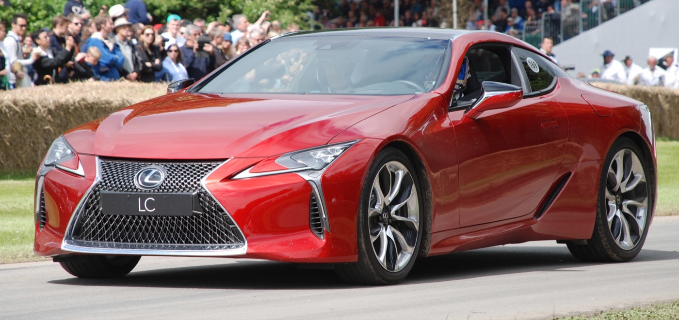 Red Lexus LC 500 with an LC plate on the grille driving on the Goodwood hill course past spectators