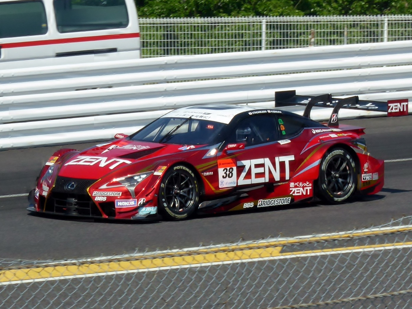 Red and white No. 38 ZENT Cerumo Lexus LC 500 GT500 racing car with a large rear wing on the track at Suzuka