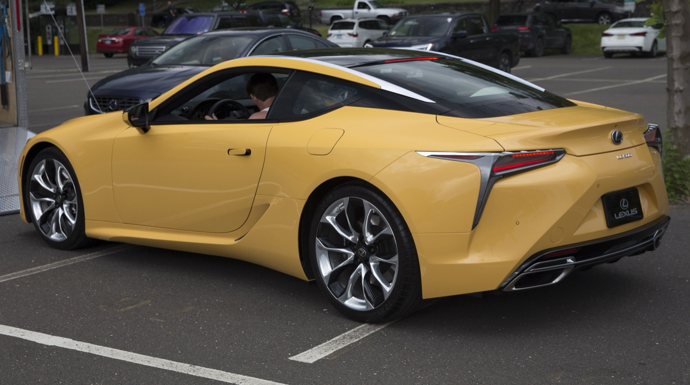 Yellow Lexus LC 500 coupe seen from the rear quarter, showing its tail lamps and twin exhausts in a car park