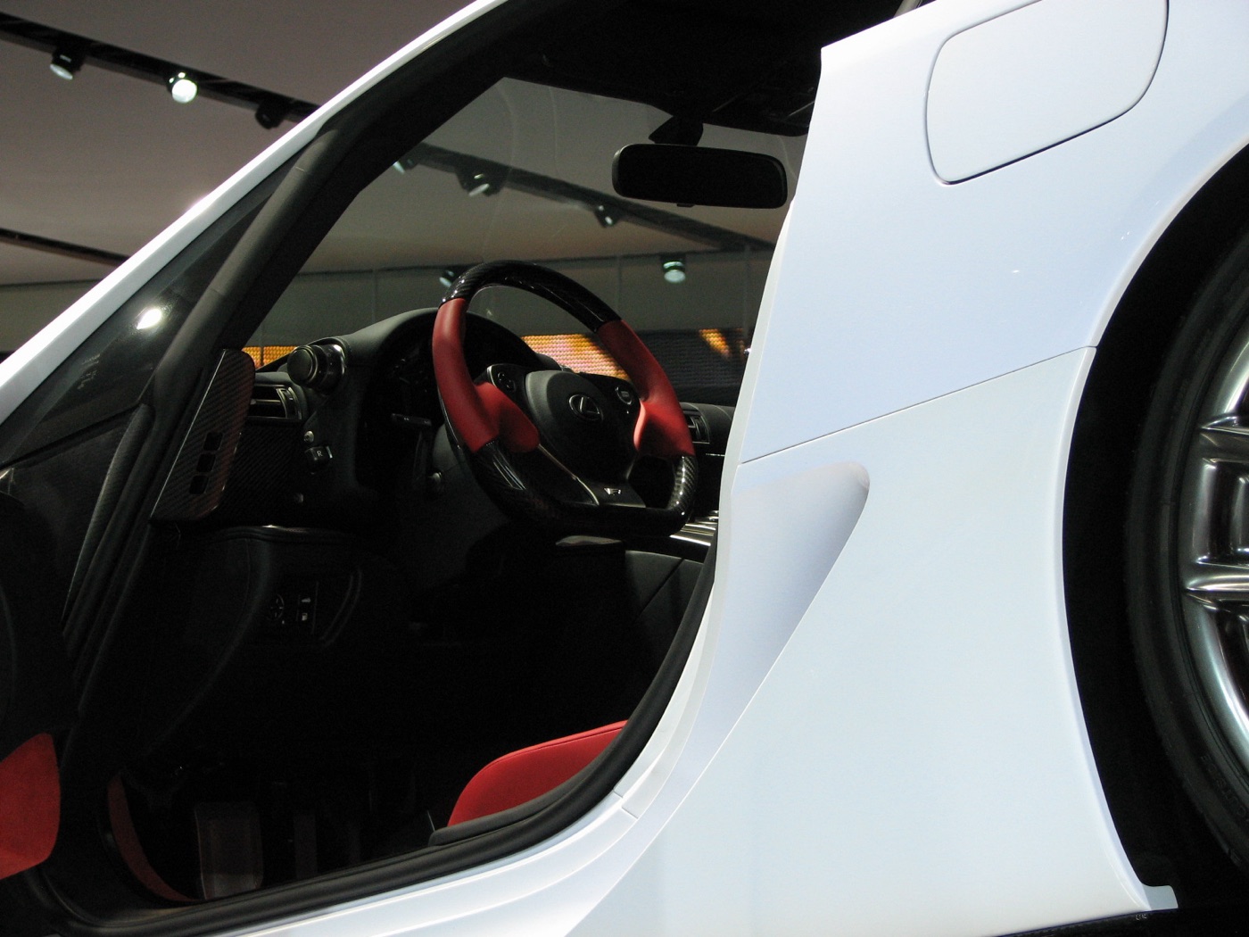 View through the open door of a white Lexus LFA to its red and black steering wheel and red seats