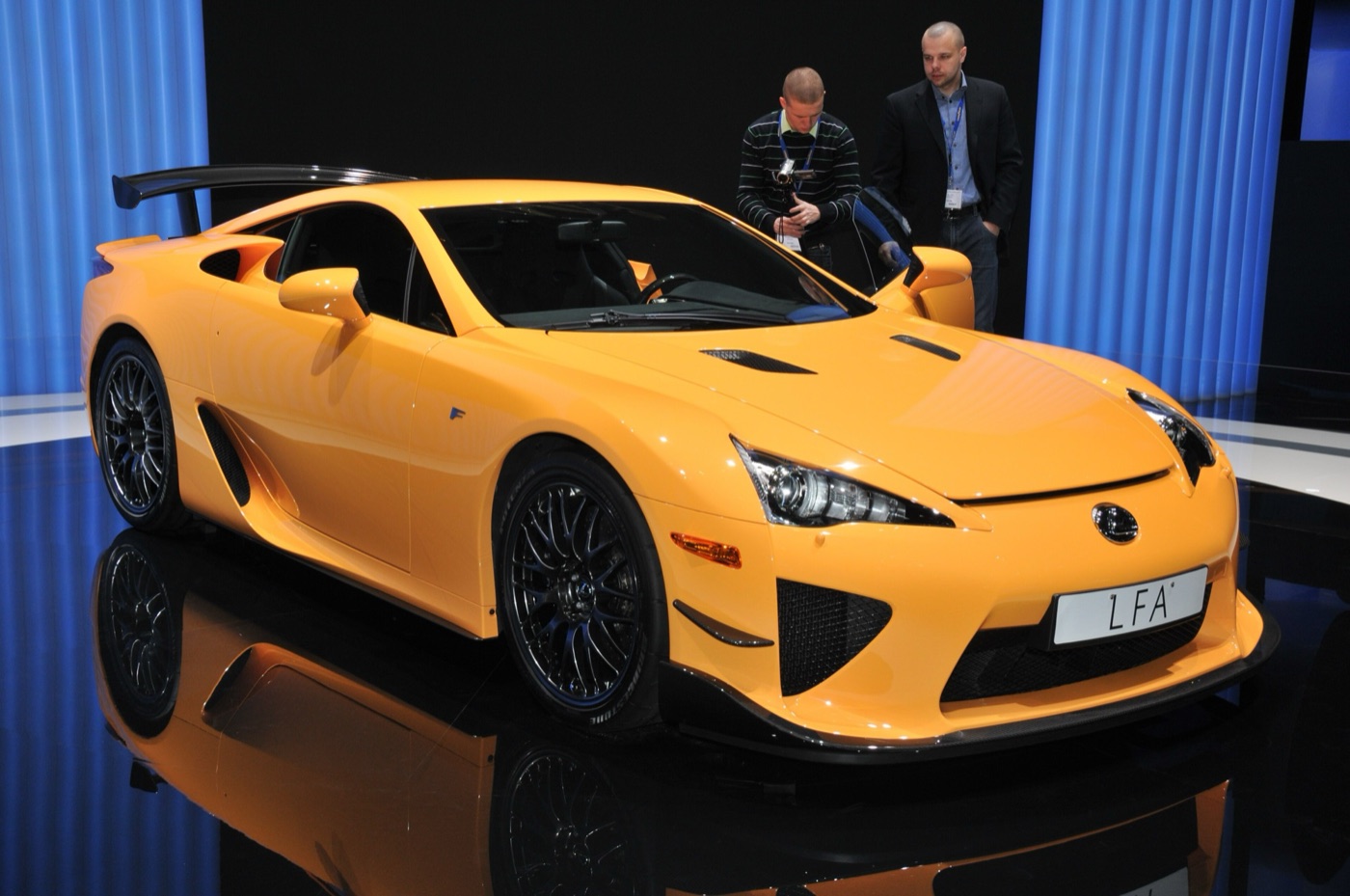 Orange Lexus LFA Nurburgring Package with a fixed rear wing and black mesh wheels on a motor show stand