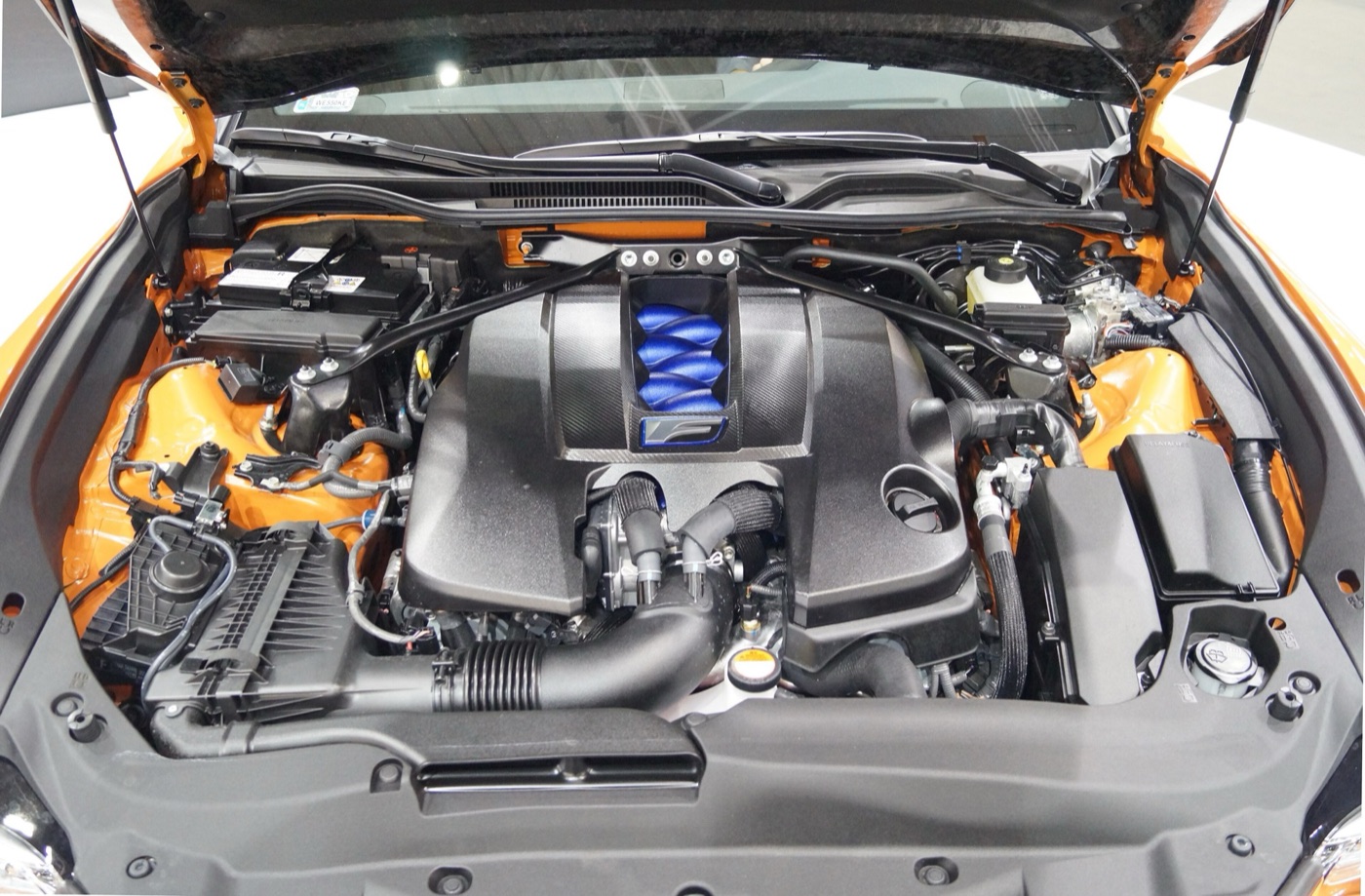 Engine bay of an orange Lexus RC F with the 5.0-litre V8 under a black cover and blue intake runners showing