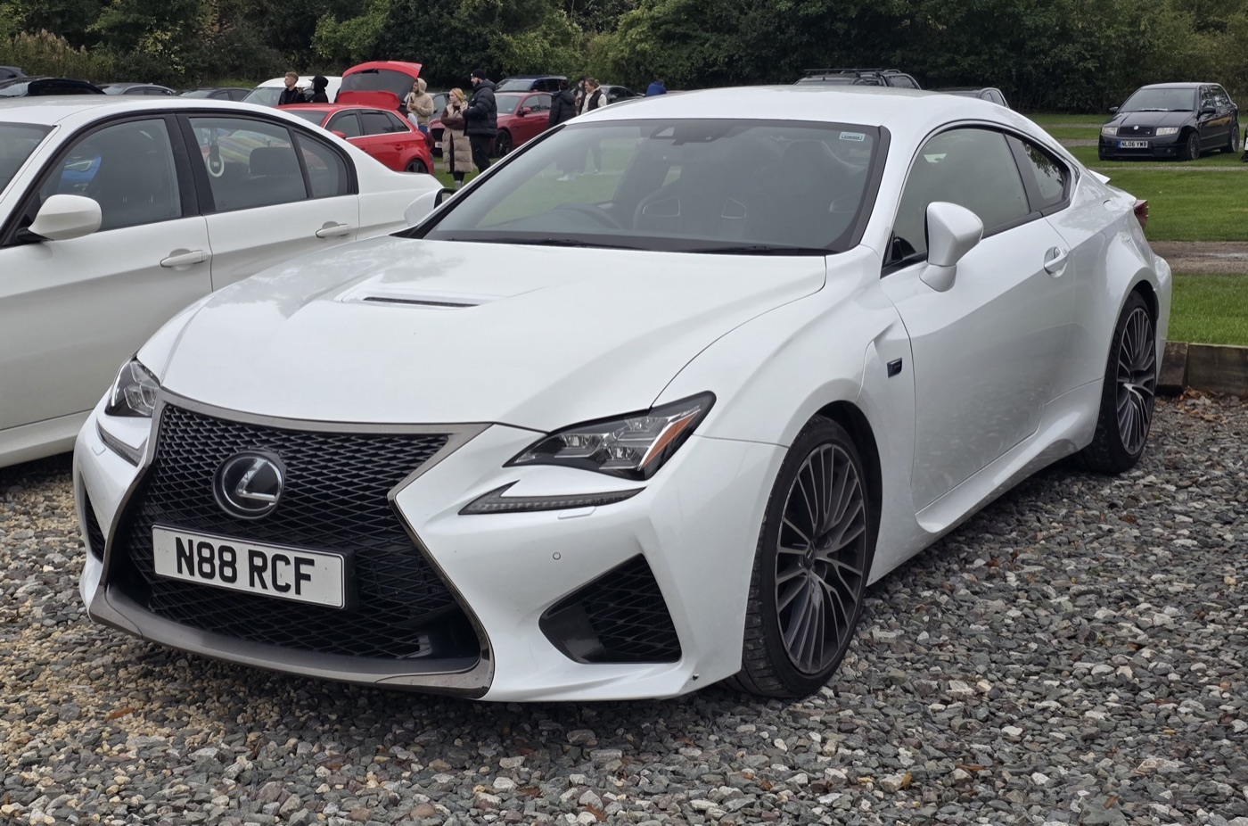 White right-hand-drive Lexus RC F coupe seen from the front three-quarter, parked on gravel at a car show