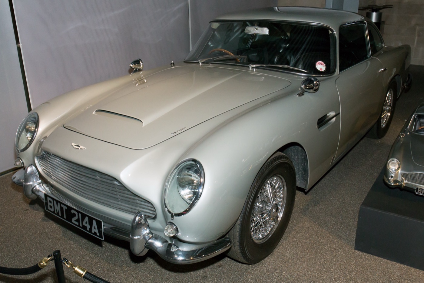 Silver Aston Martin DB5 with wire wheels and the number plate BMT 214A, one of James Bond's cars, on display behind a rope