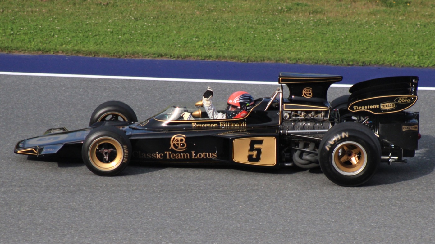 Black and gold Lotus 72D with Emerson Fittipaldi's name and Classic Team Lotus lettering, number 5, on track with the driver waving