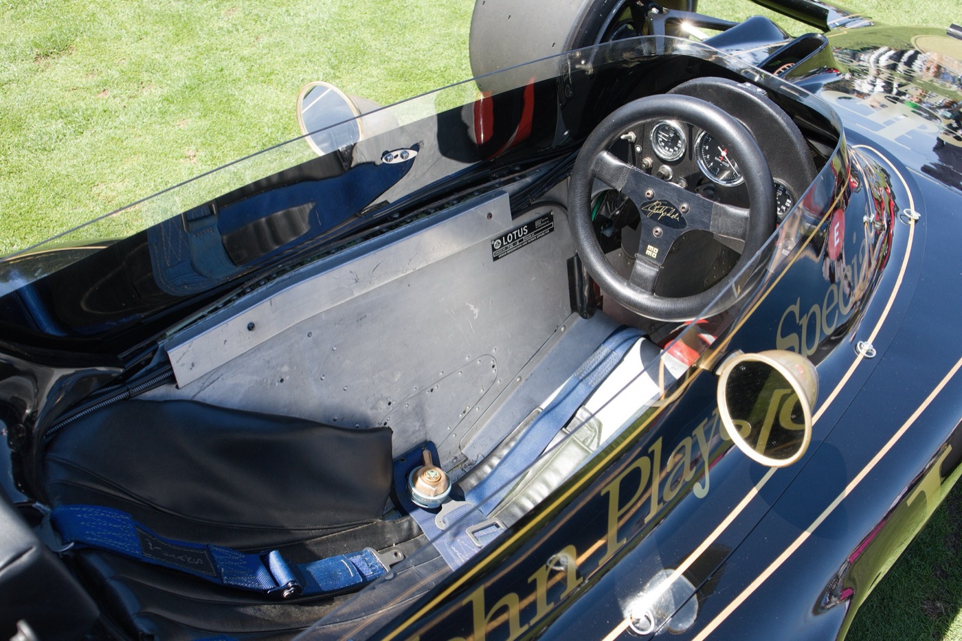 Cockpit of a Lotus 72E with a black steering wheel, three dials, an aluminium bulkhead and blue harness straps