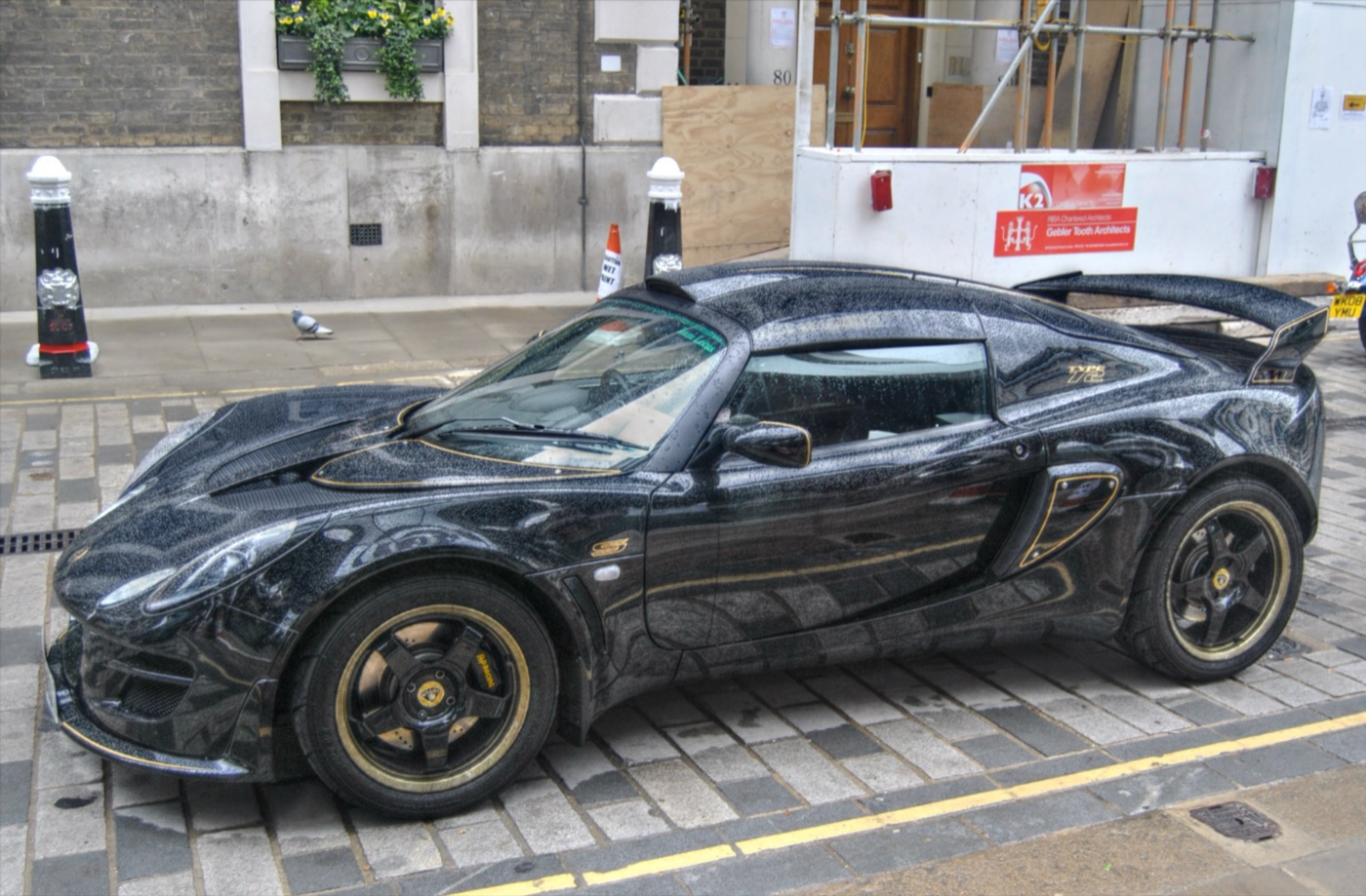 Black Lotus Exige S Type 72 with gold-rimmed black wheels and gold Type 72 lettering, parked in a London street