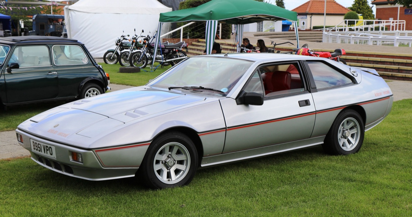 Silver Lotus Excel coupé with red pinstripes and red interior parked on grass at a show