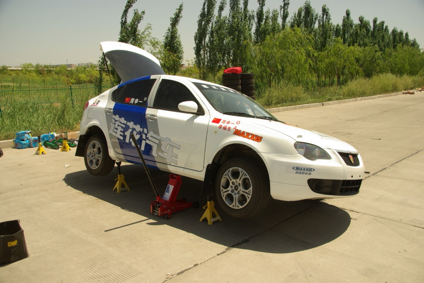 White Youngman Lotus L3 hatchback rally car with Chinese lettering on jacks in a service area