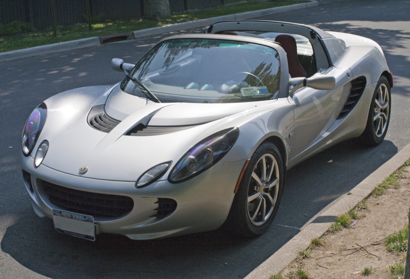 Silver 2005 Lotus Elise with a black targa roof frame and New York number plate, parked at a kerb