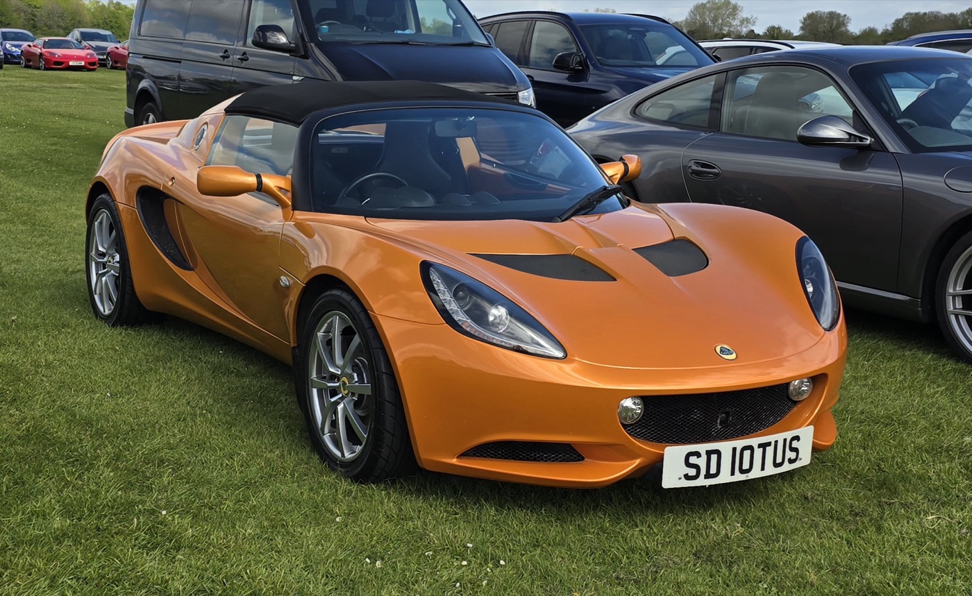 Orange 2010 Lotus Elise R with a black roof, the facelifted Series 3 shape, parked on grass