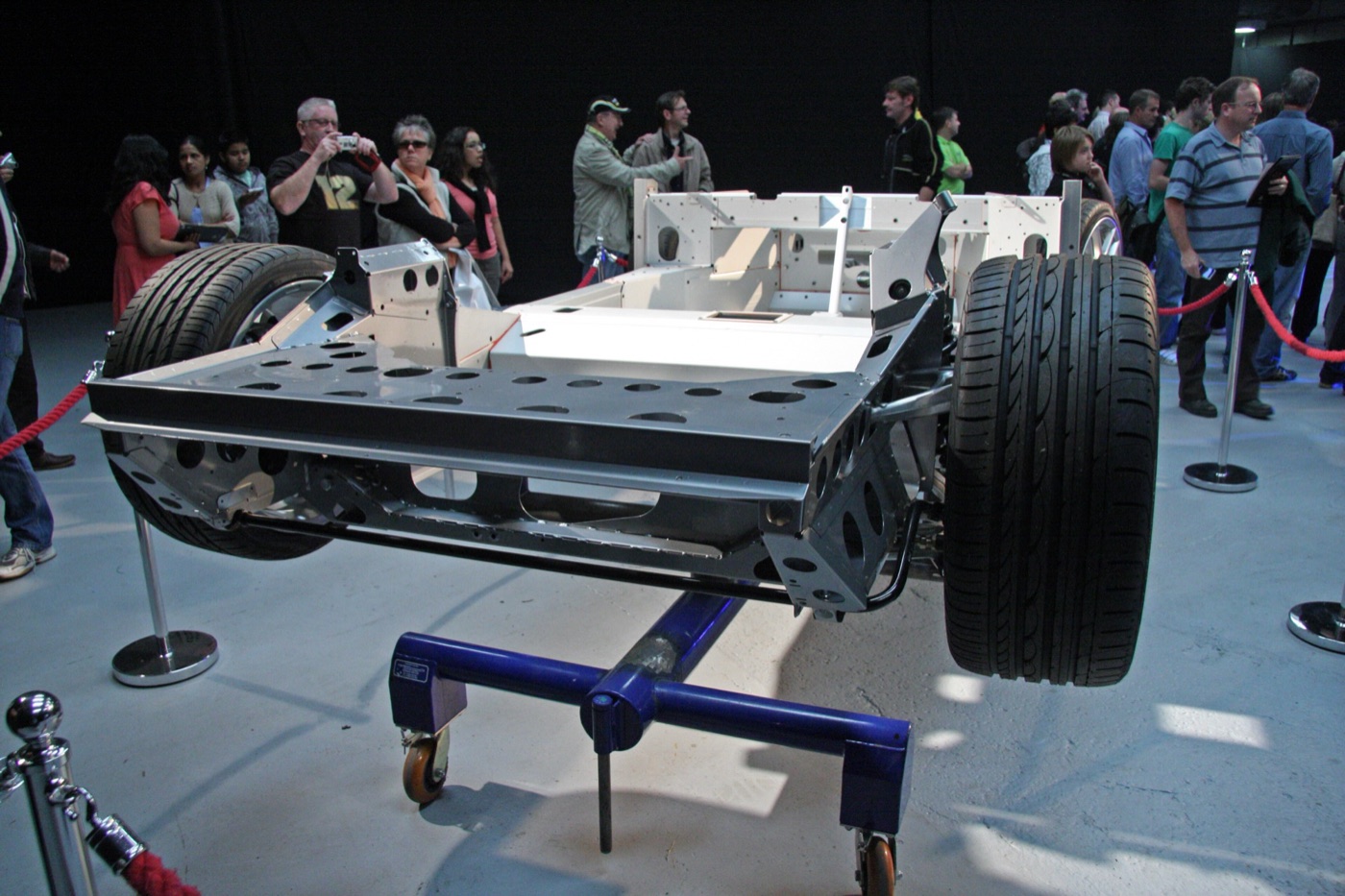 Bare bonded aluminium chassis tub of a Lotus Evora with wheels fitted, on a display stand