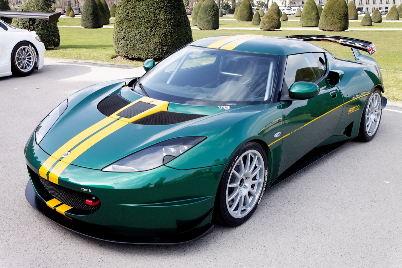 Green Lotus Evora GT4 race car with yellow stripes and a rear wing, parked on gravel