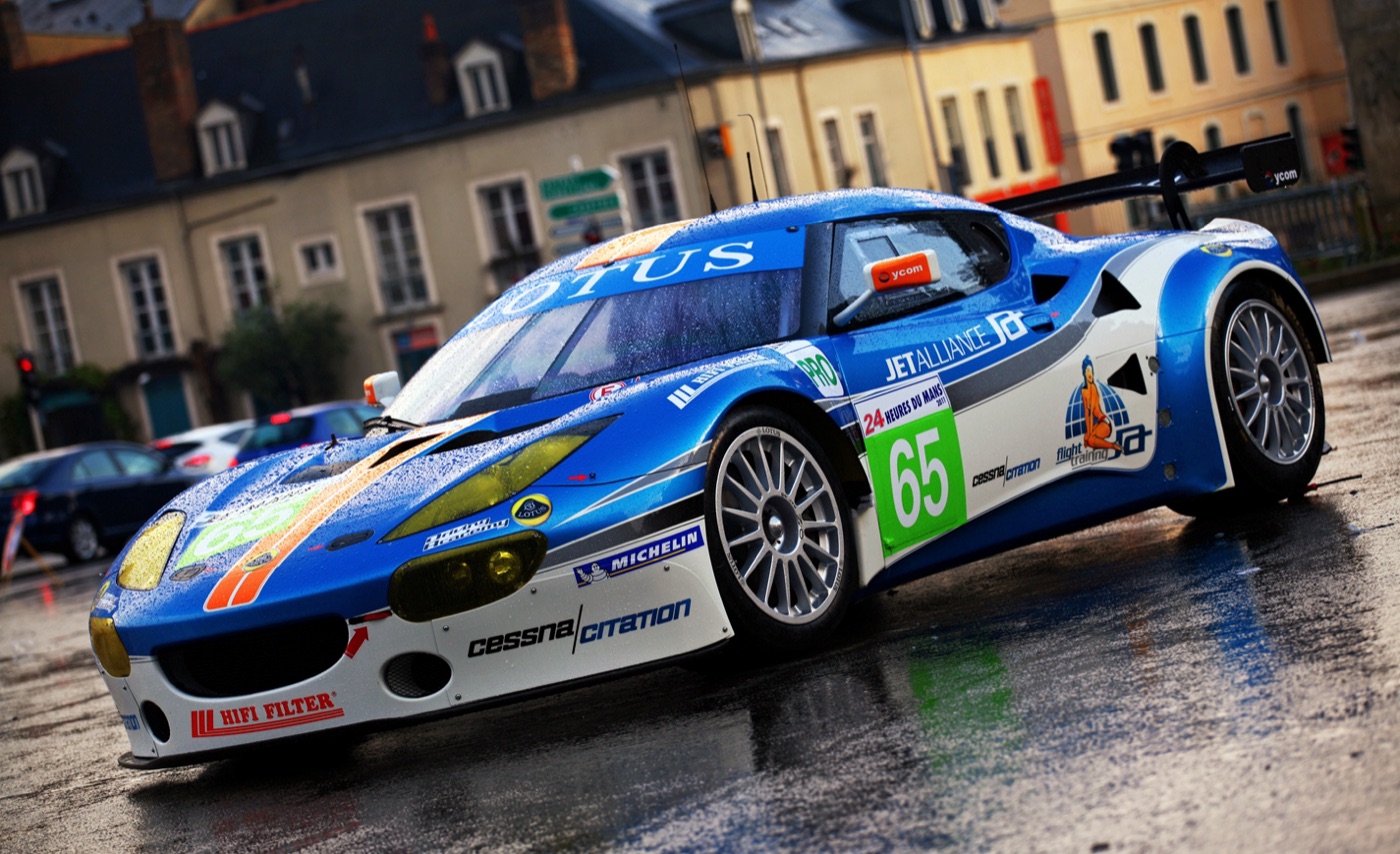 Blue and white Jetalliance Lotus Evora GTE race car number 65 on a wet town square