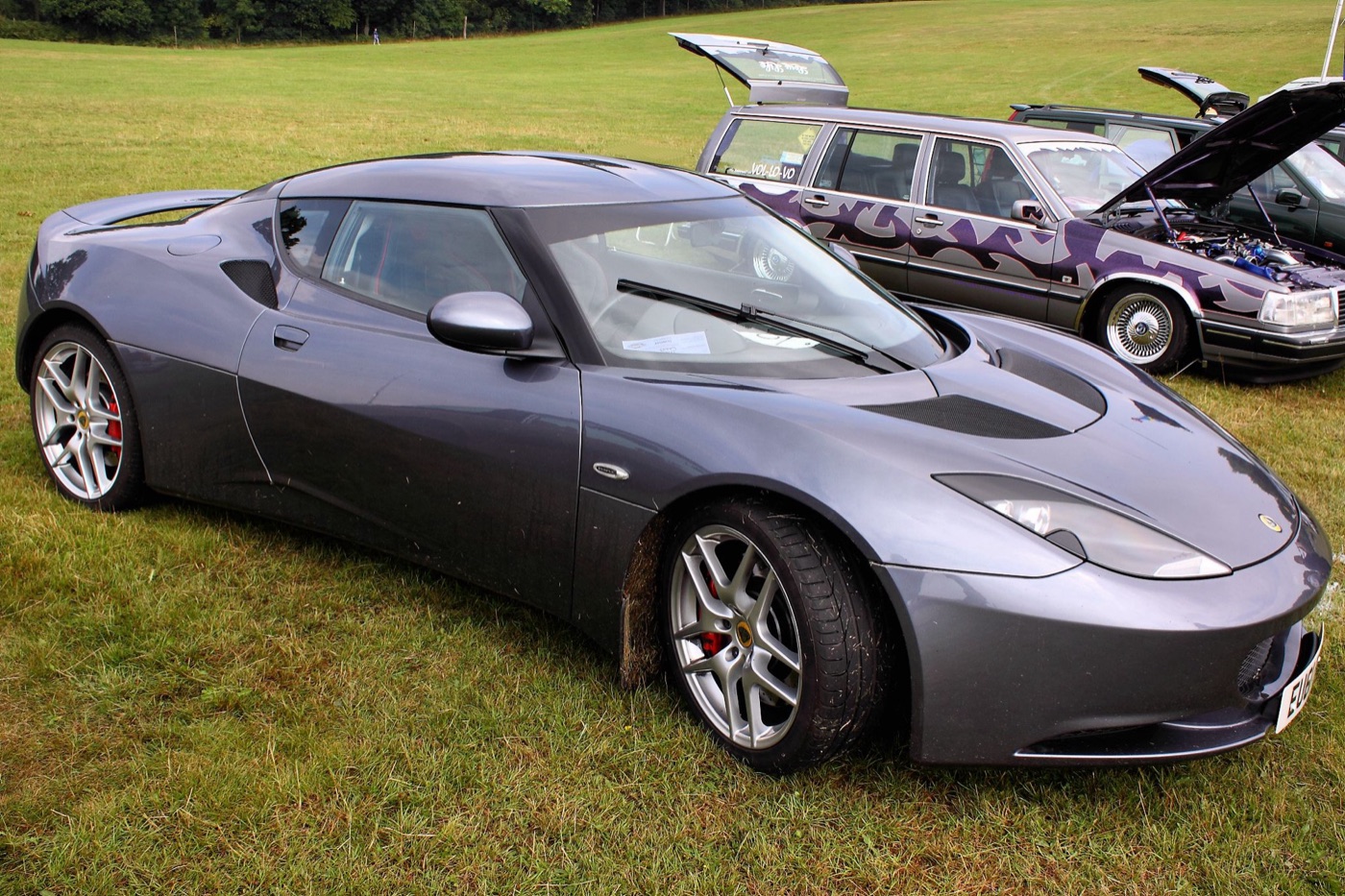 Grey Lotus Evora parked on grass at a car show, with other cars behind