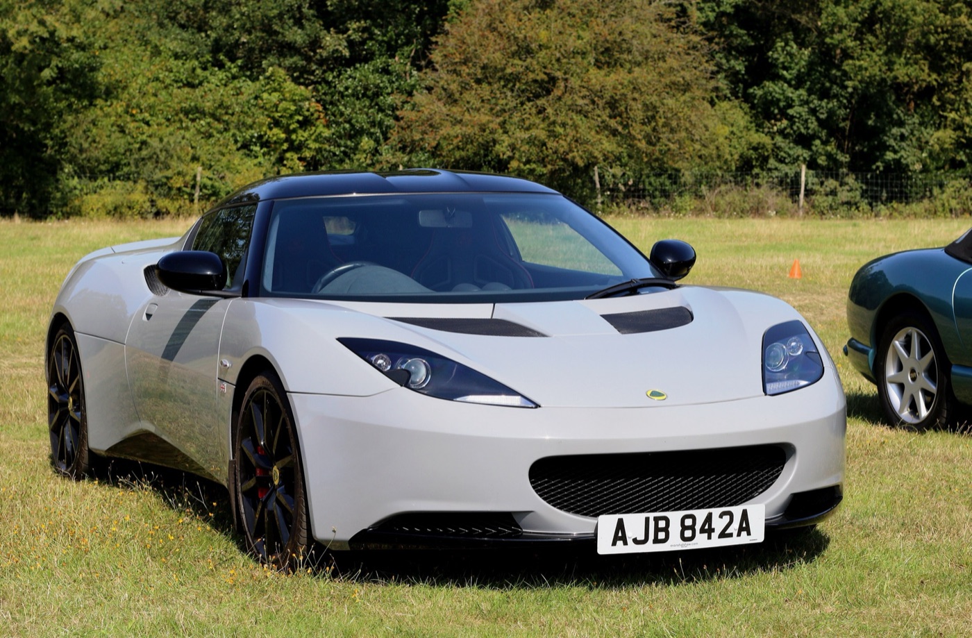 White Lotus Evora S with black roof and dark wheels parked on grass, seen from the front three-quarter