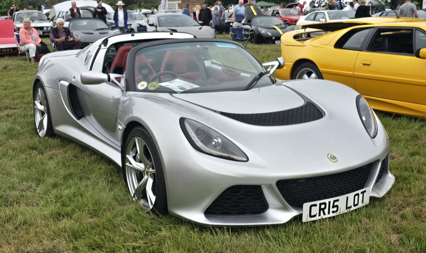 Silver Lotus Exige S Roadster with black soft top and red leather seats, parked on grass
