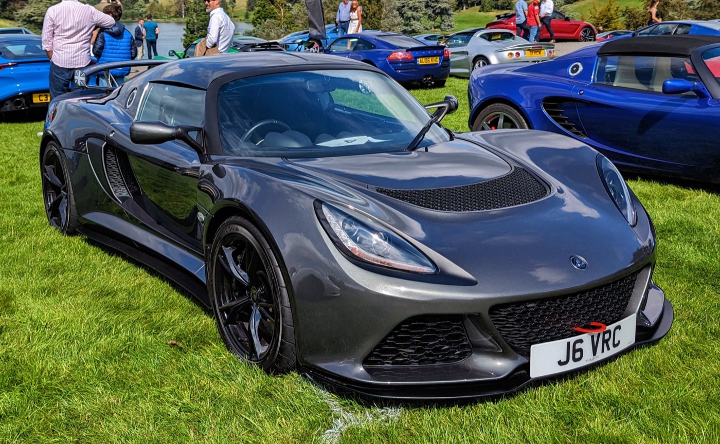 Dark grey Lotus Exige S V6 coupé with black wheels, parked on grass at a car show