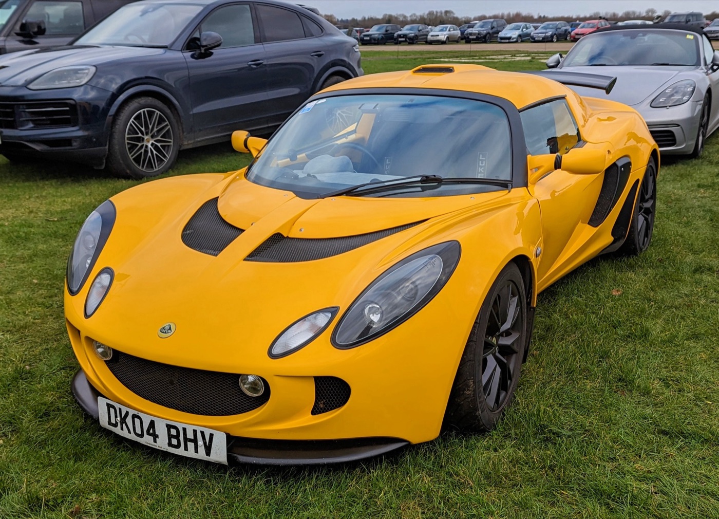 Yellow Lotus Exige Series 2 coupé with roof scoop and front splitter, parked on grass