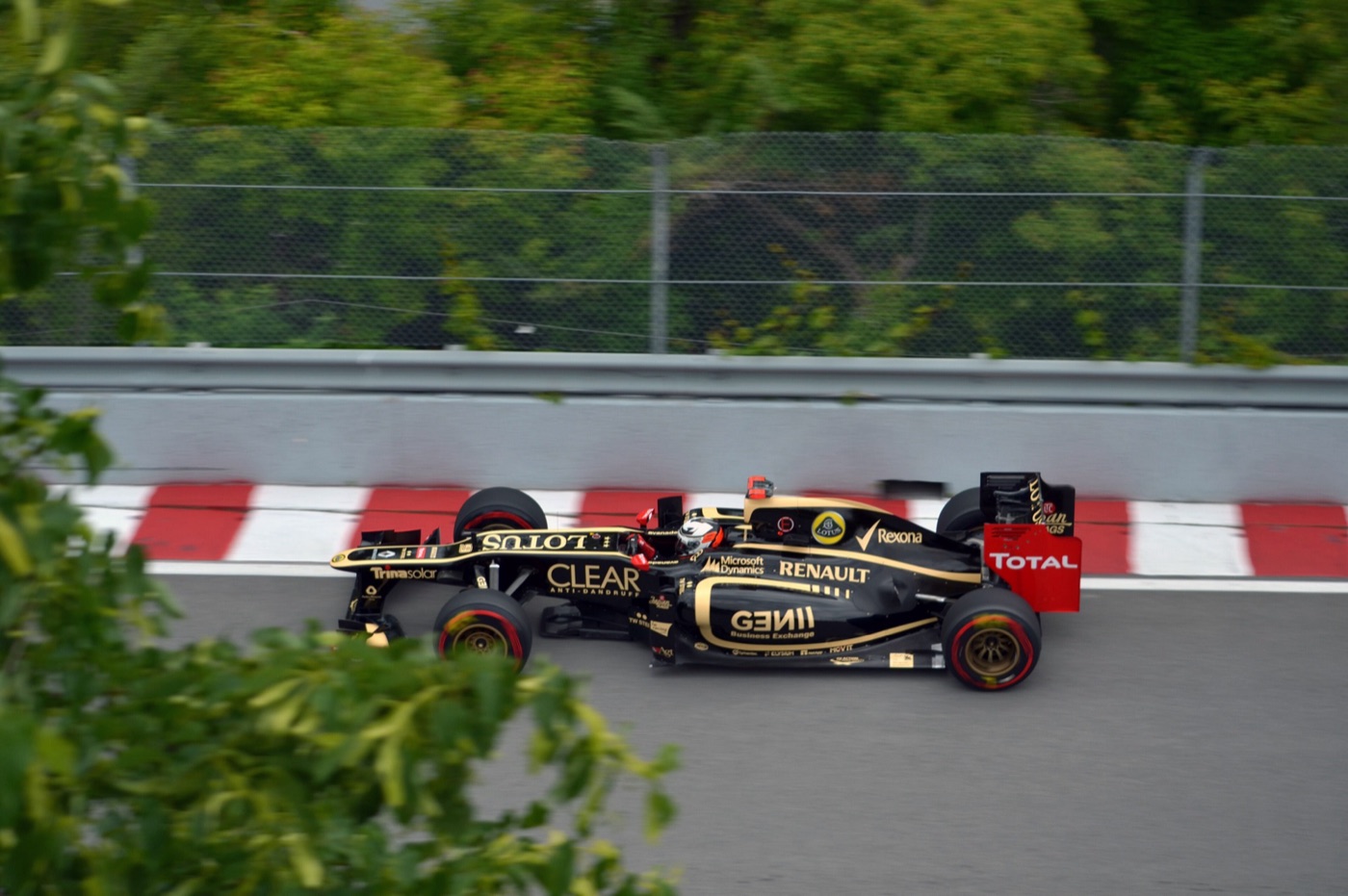 Black and gold Lotus E20 with Genii, Clear and Renault logos on track beside a red and white kerb