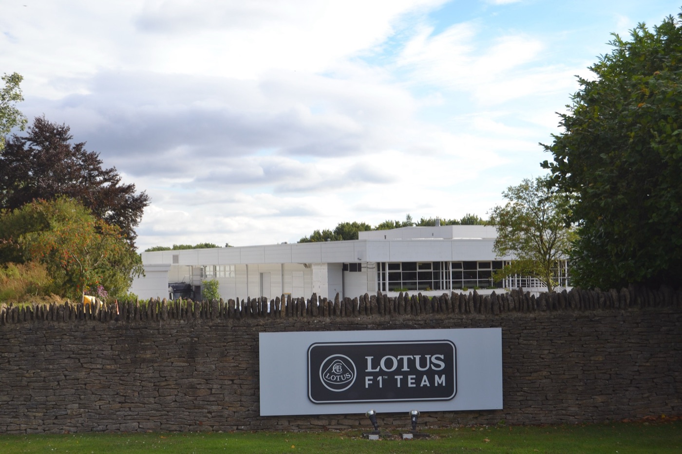 Low white factory building behind a dry-stone wall with a Lotus F1 Team sign in black and gold