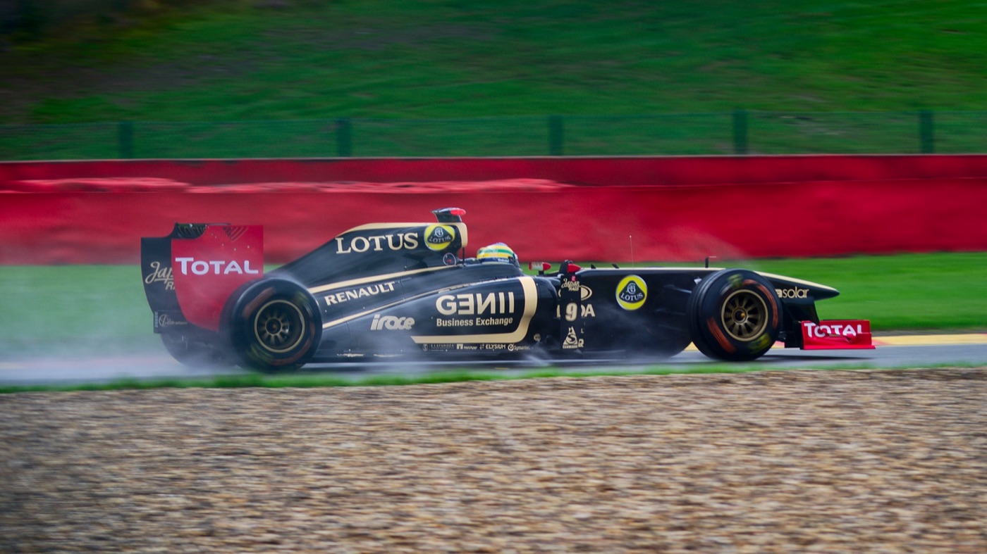 Black and gold Lotus Renault R31 throwing up spray on a wet track beside a red and green kerb