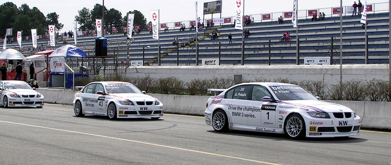 Three white BMW 320si touring cars in the pit lane, the nearest numbered 1 with A. Priaulx on the window and BMW Team UK on the door