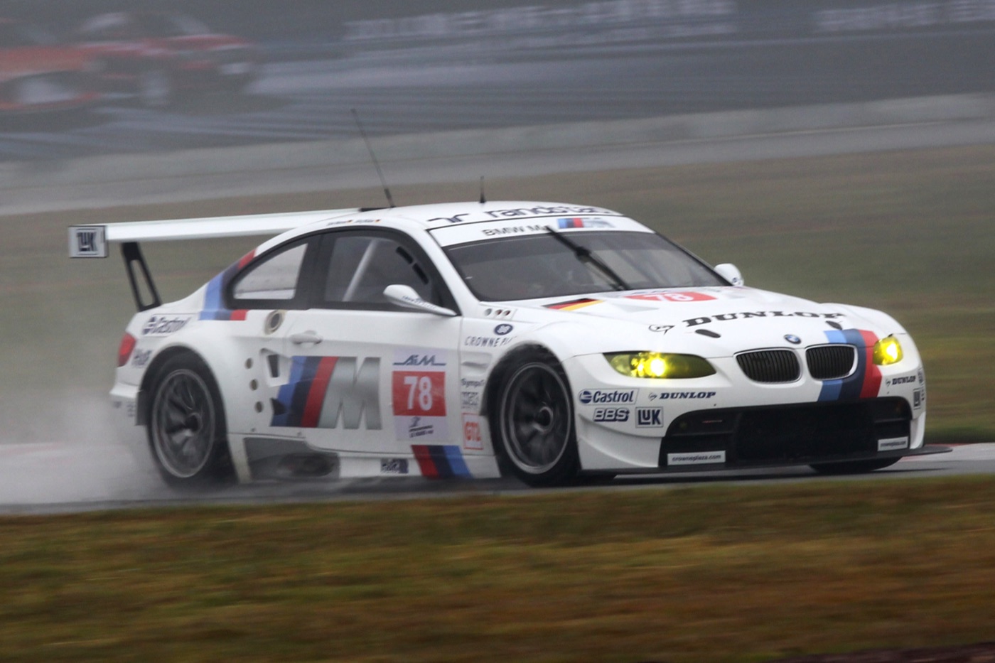 White BMW M3 GT2 racing car, number 78, with M stripes and Dunlop and Castrol lettering, throwing up spray on a wet track