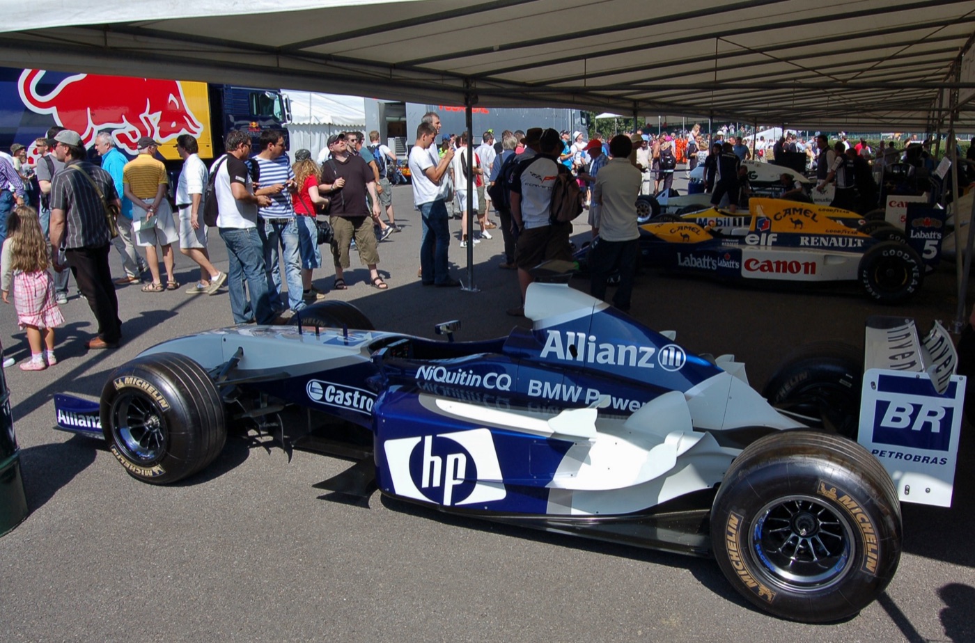 Blue and white Williams FW25 Formula One car with Allianz, HP and BMW Power lettering, parked under an awning in a crowded paddock