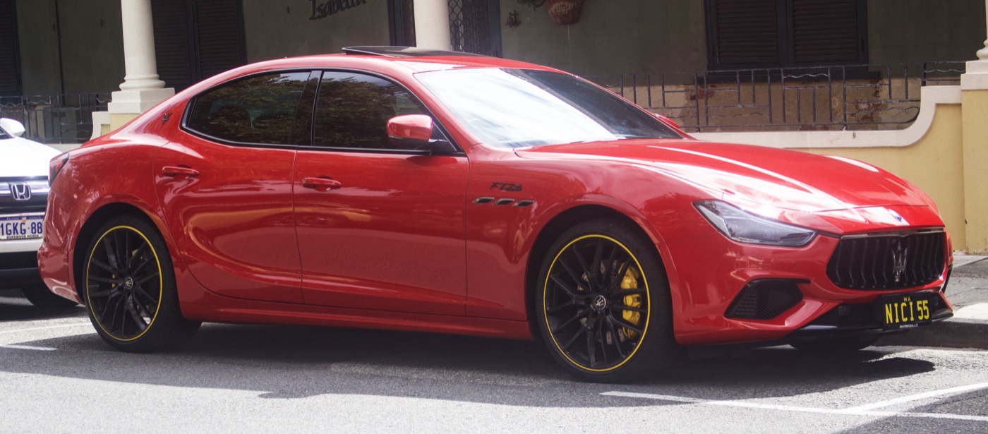 Red Maserati Ghibli FTributo Special Edition with black wheels and yellow pinstripes on the rims, parked beside a colonnaded building